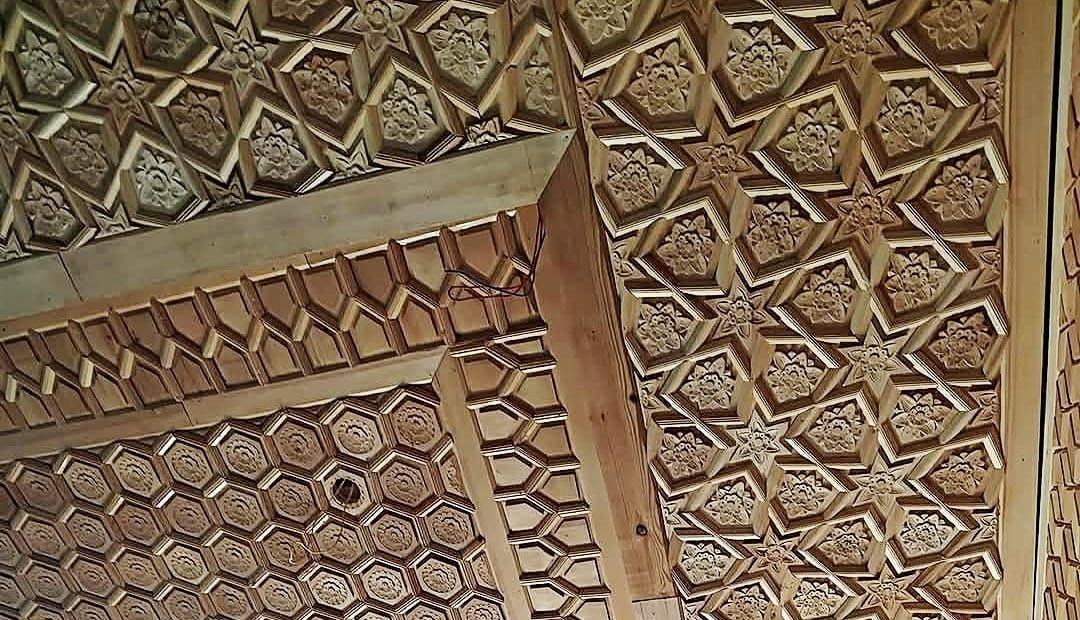 Bare unpainted khatamband ceiling in Kashmiri silver fir, hundreds of hand-cut wooden stars and hexagons interlocked without nails or glue.