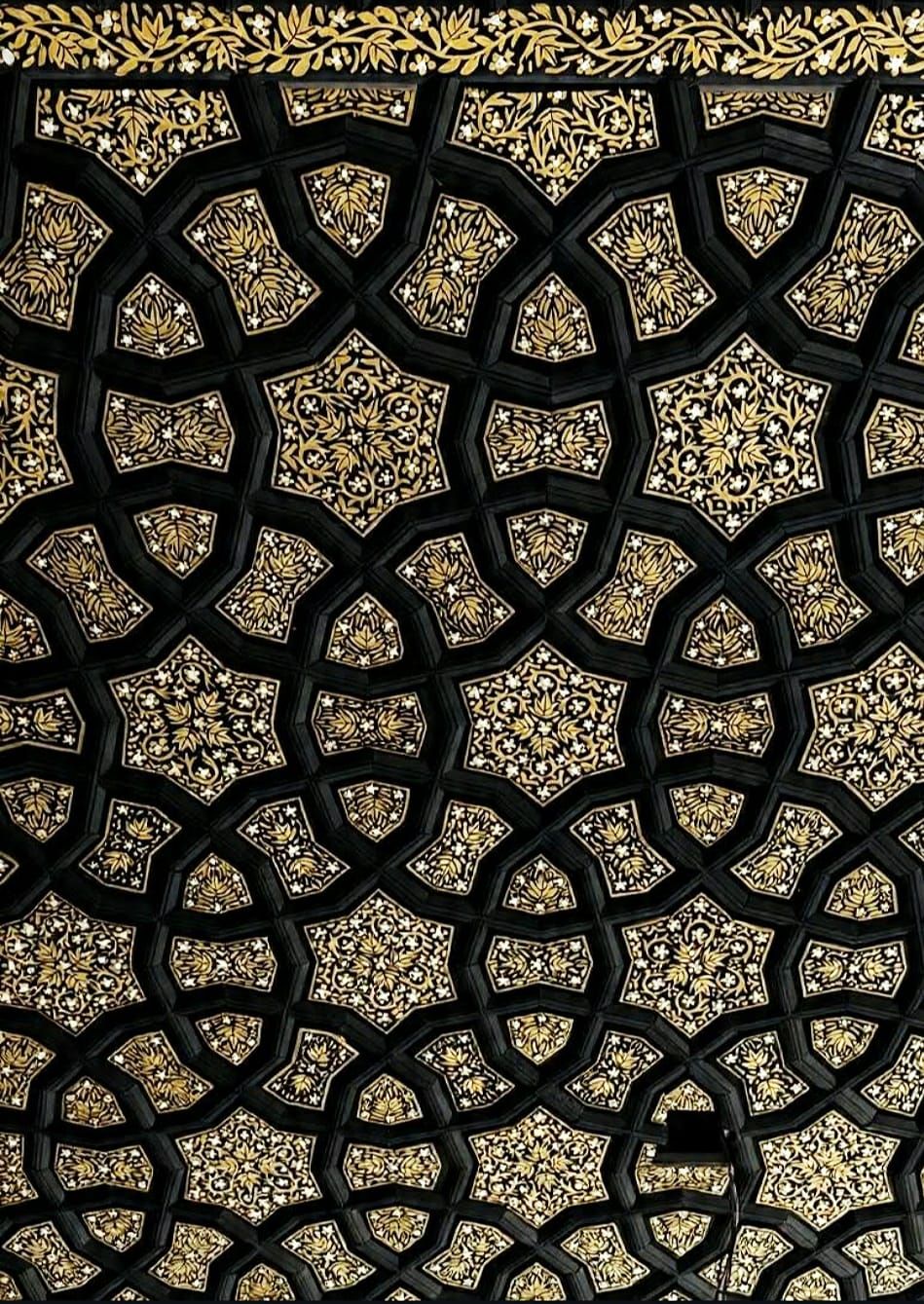 Close view of paper machie naqashi painted onto a khatamband ceiling, gold floral motifs on a black lacquer ground with fine white blossom.