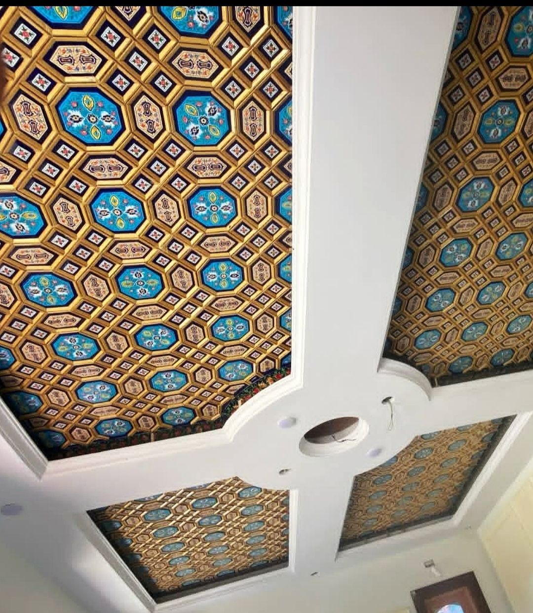 Khatamband ceiling of gold-edged octagons with turquoise paper machie panels running across white beams in a Srinagar house.
