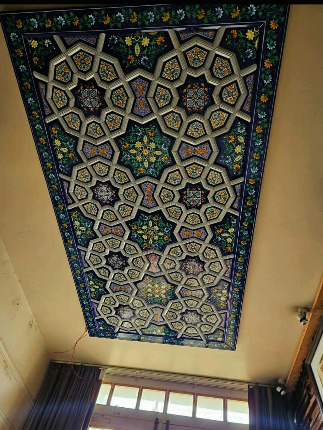Rectangular khatamband hall ceiling with pale interlocking stars on a navy ground and a painted floral vine border.