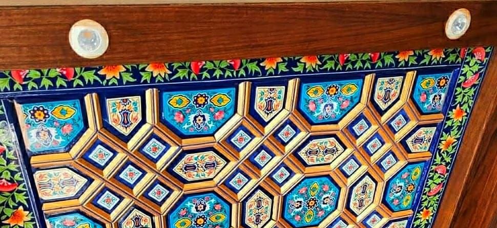Khatamband ceiling of gold octagons on turquoise, framed by walnut beams and a painted pomegranate vine border.