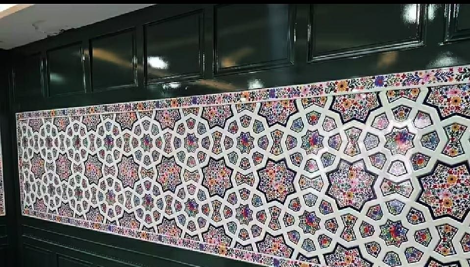 Long khatamband wall panel of white interlace filled with dense multicoloured paper machie flowers, set into dark green panelled joinery.