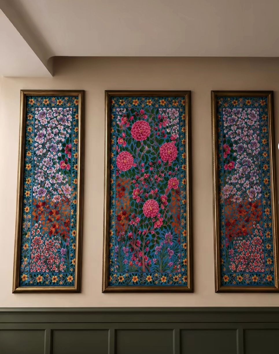 Three tall paper machie wall panels on a teal ground painted with pink dahlias and blossom in gold frames.